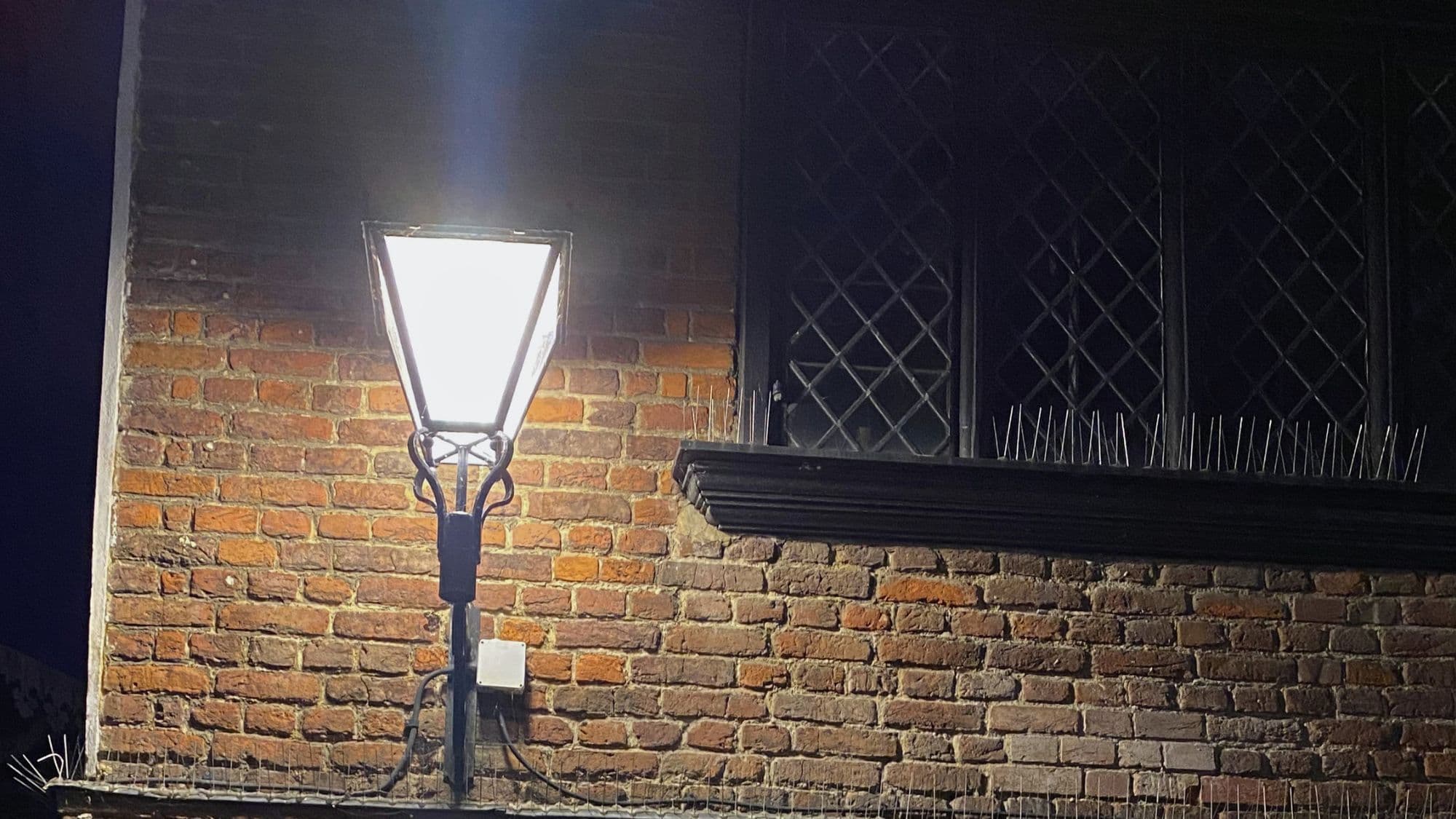 Historic brickwork and leaded windows of Eastgate House in Rochester illuminated by a streetlamp at night.